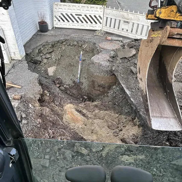 Dyp utgraving foran bolig, sett fra innsiden av en gravemaskin.