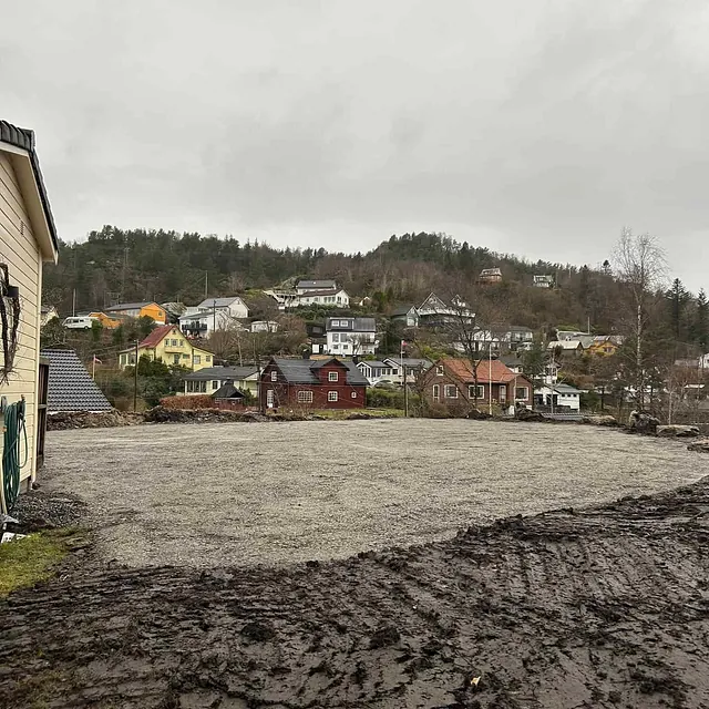 Gruslagt og planert tomt foran rekke hus i bakkelandskap en overskyet dag.